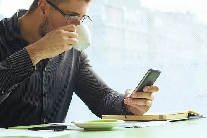 man drinking coffee and reading cell phone