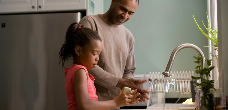 father helping daughter wash hands at the kitchen sink